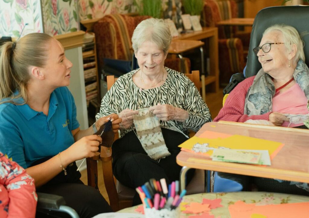 Care home worker knitting with residents