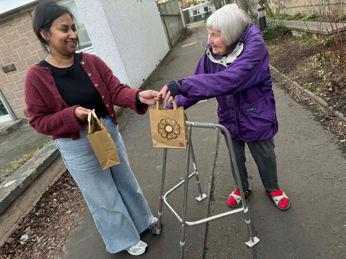 care home resident with walker outside handing gift bag to local woman