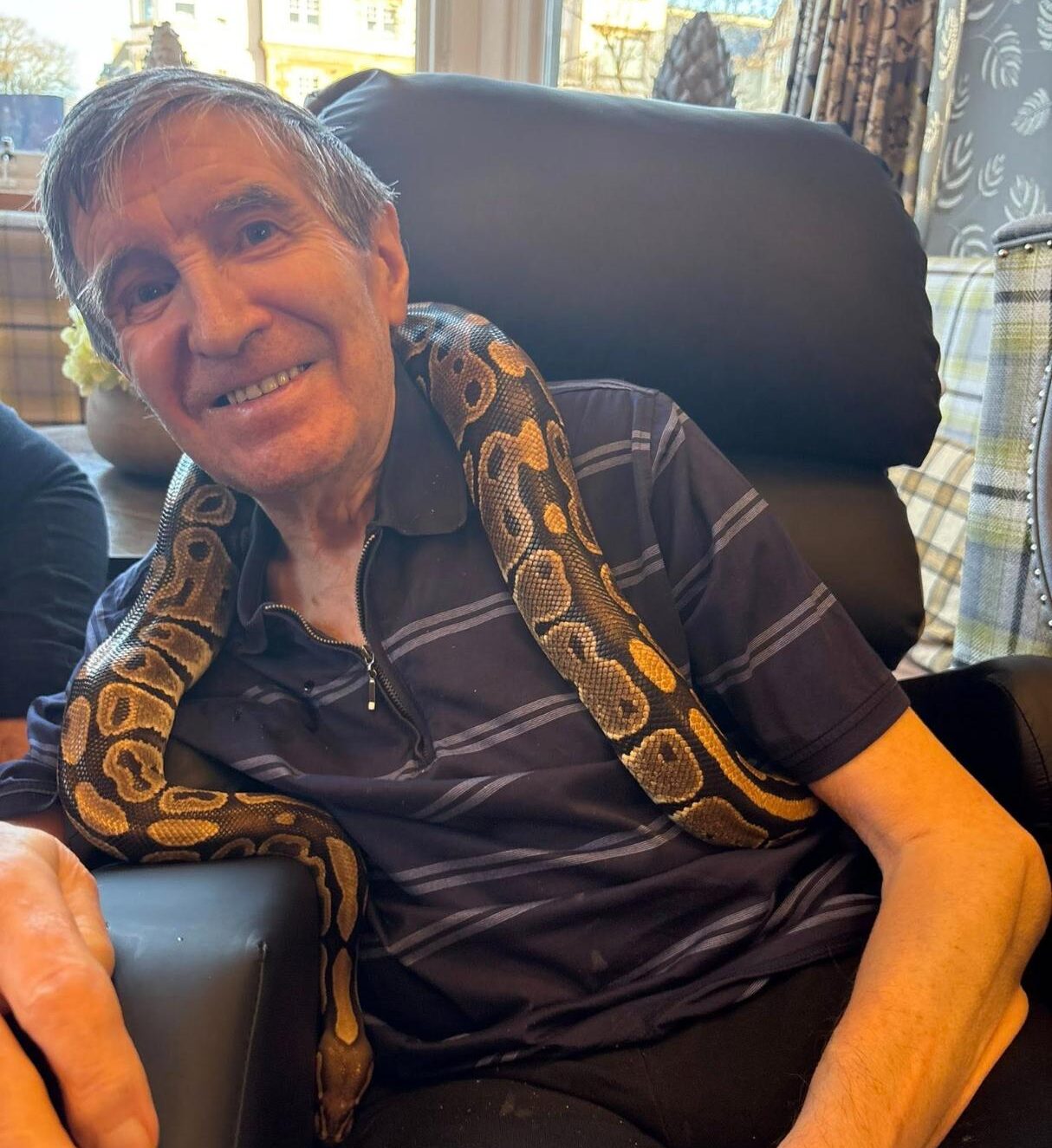 care home resident smiling with a snake therapy pet round his shoulders