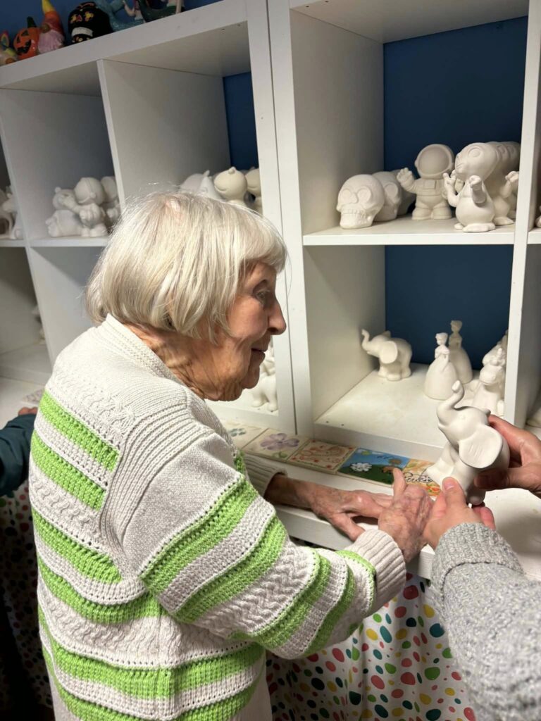elderly woman looking at a shelf of white ceramic items to paint