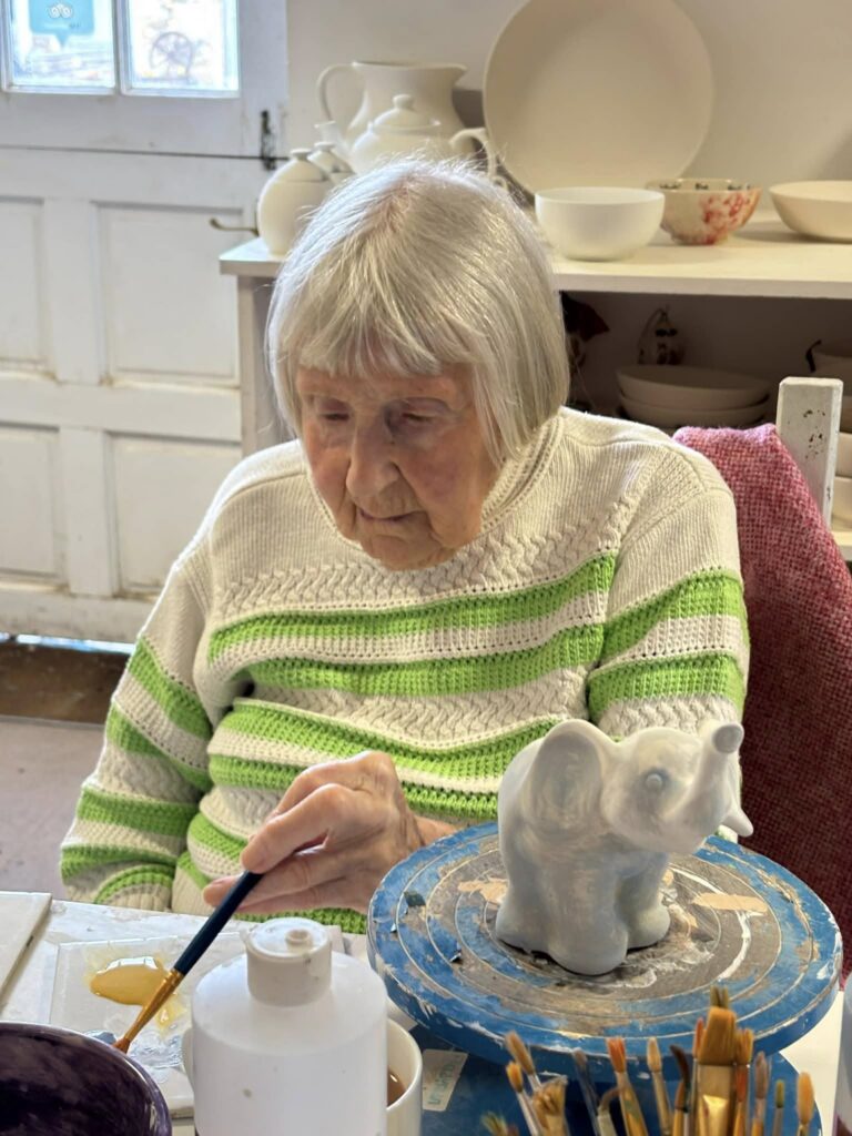 elderly woman painting a ceramic blue elephant