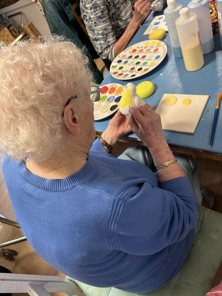 elderly woman painting a yellow ceramic bird